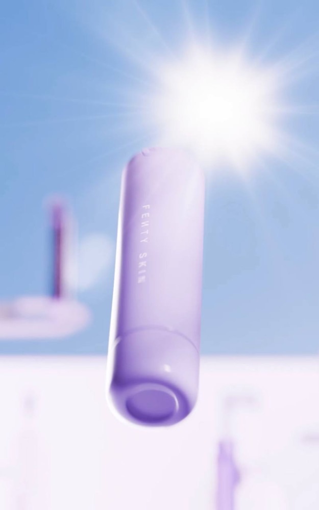 A purple Fenty Skin tube floats against a bright blue sky with a glowing sun flare