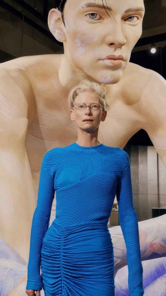 Tilda Swinton posed infront of a giant, hyper-realistic robotic sculpture