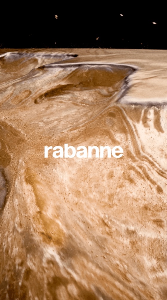 A close-up of a swirling, liquid gold texture with the "rabanne" logo centered