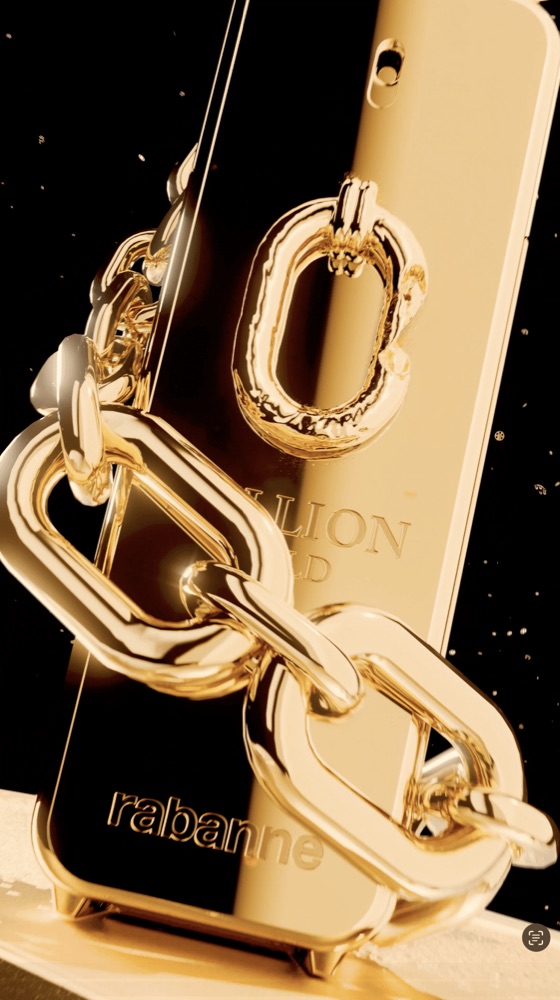 A tight shot of a chunky, polished gold chain draped over a metallic Rabanne fragrance bottle