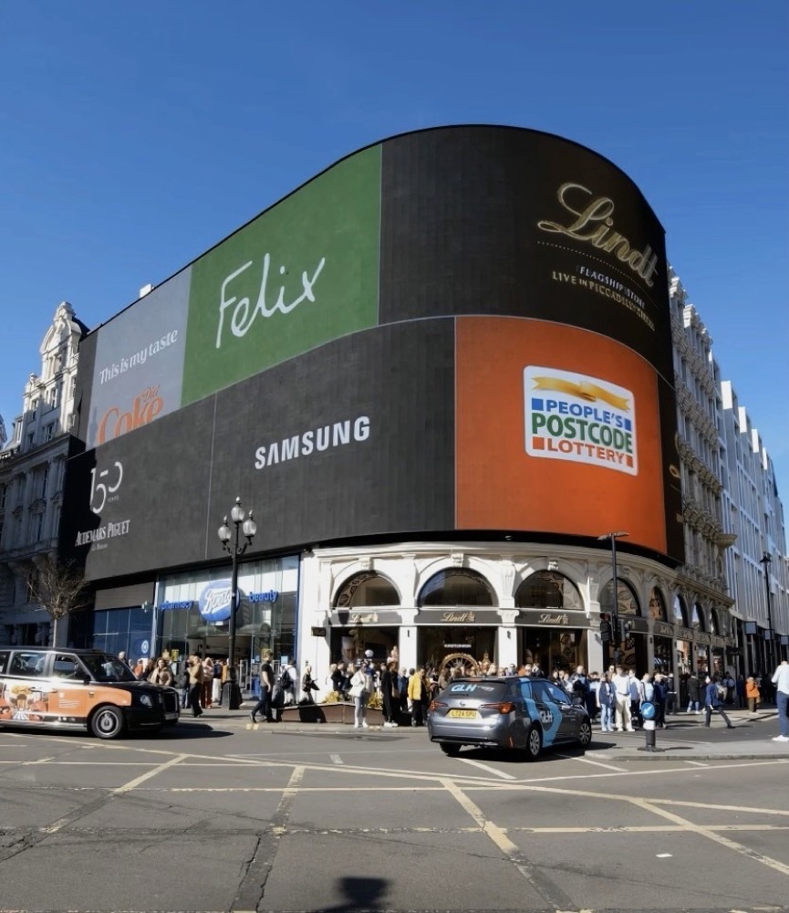A wide photograph of Piccadilly Circus serves as the empty base plate for the digital assets